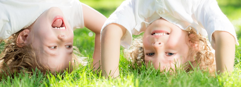 Happy children standing upside down on green grass in spring park. Healthy lifestyles concept.